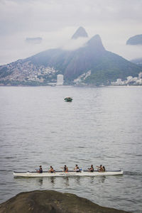 People on boats in sea against mountain