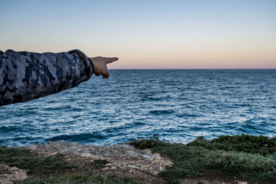 Cropped image of person pointing at sea against sky during sunset