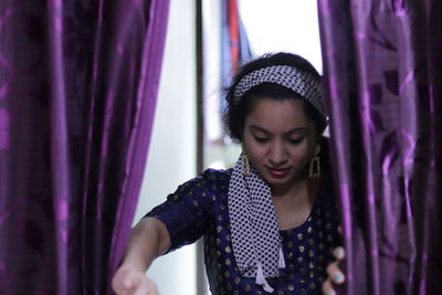 Portrait of beautiful young woman standing against purple curtain