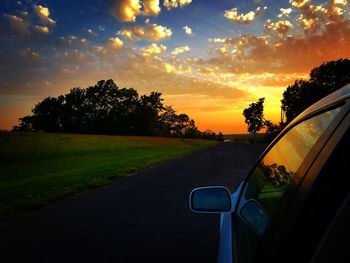 Road by trees against sky during sunset