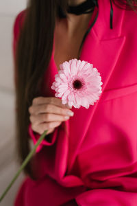 Close up of a pink gerbera flower in the hands of a young woman in fuchsia-colored clothes