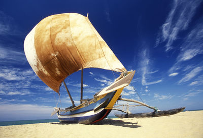 Outrigger boat moored at beach during sunny day