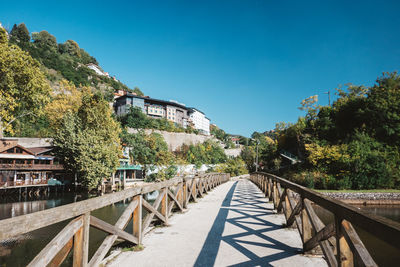 Footbridge amidst trees against clear blue sky