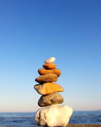 Stack of stones in sea against clear blue sky