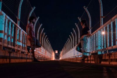 Side view of people standing on bridge against sky in city at night