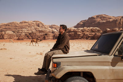 Thoughtful young man sitting on car in desert