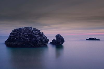 Rocks in sea against sky during sunset