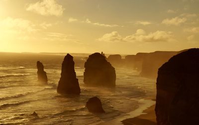 Silhouette rocks on shore against sky during sunset