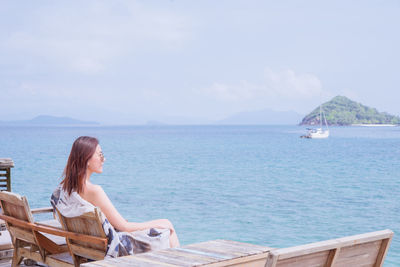 Woman sitting on bench looking at sea against sky
