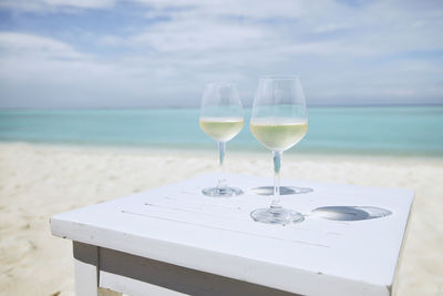 Two wineglass with white wine on wooden table against idyllic beach and turquoise sea.
