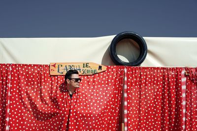 Man hiding behind red curtain against clear sky