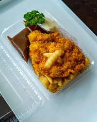 Fried chicken chop, chicken coated in breadcrumbs and fried in a takeout plastic container.