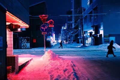 People walking on illuminated street amidst buildings in city at night