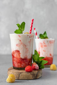 Strawberry and raspberry smoothies in glasses garnish with mint and raspberry on wooden board.