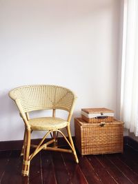 Empty chair by wicker box against wall at home