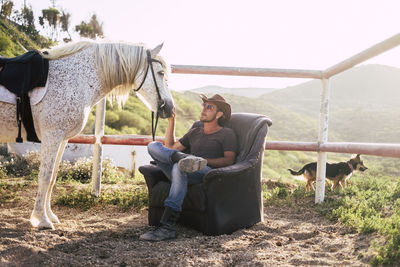 Cowboy stroking horse while sitting on armchair at ranch
