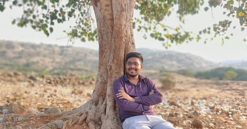 Man with arms crossed sitting under tree