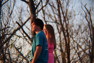 Side view of a couple standing against bare trees