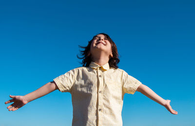 Smiling boy with arms outstretched standing against blue sky