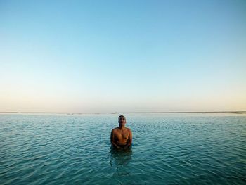 Portrait of shirtless mid adult man standing in sea against clear sky
