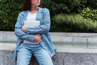 Anonymous redhead businesswoman holding a laptop outdoors. background with plants