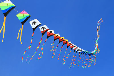 Low angle view of kites flying in clear blue sky