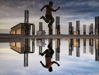 Symmetric view of man jumping by puddle against sky