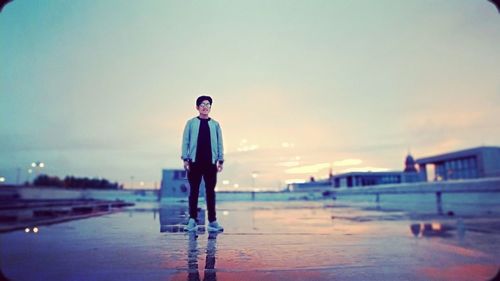 Full length portrait of young man standing at swimming pool against sky