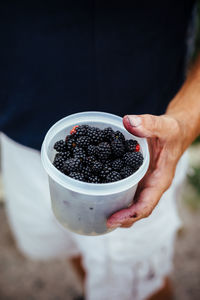Midsection of man holding blackberries in container
