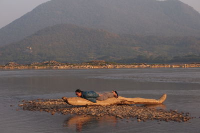 Man lying on driftwood against mountain