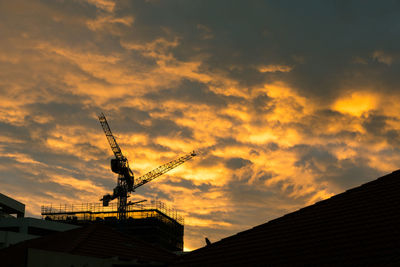 Low angle view of silhouette crane by building against sky during sunset