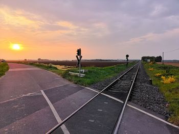 Railroad tracks by road against sky during sunset