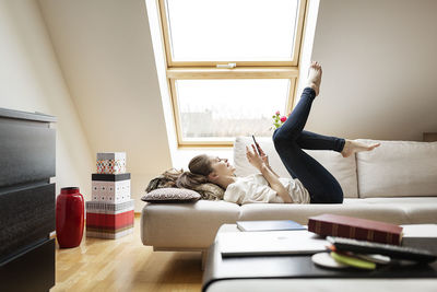 Happy woman lying on couch using cell phone