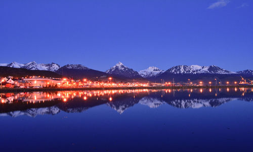 Scenic view of lake by illuminated mountains against clear blue sky at night