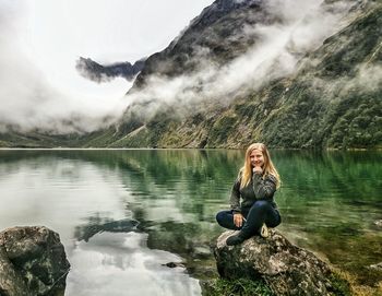 Portrait of woman sitting by lake on rock
