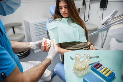 Professional doctor demonstration process of healthy teeth brushing to young woman sitting in chair.