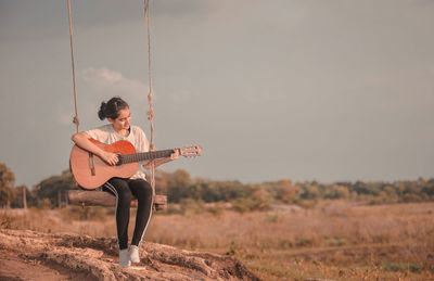 Full length of woman playing guitar on field against sky