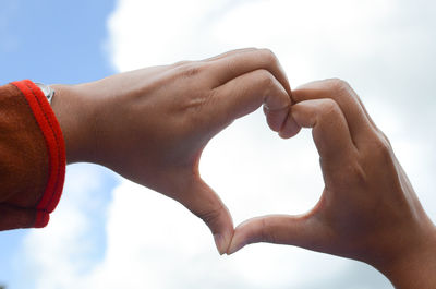 Midsection of man making heart shape against sky