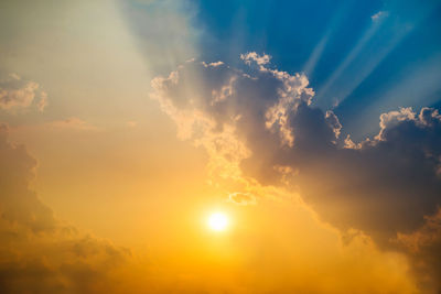 Low angle view of sunlight streaming through clouds during sunset