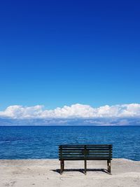 Empty bench on beach by sea against blue sky