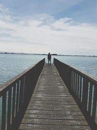 Rear view of woman standing on pier over lake against cloudy sky