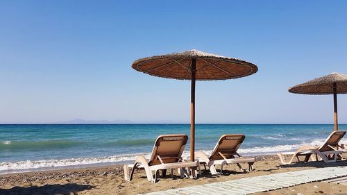 Deck chairs and parasols on beach against clear sky