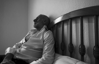 Monochrome of adult man in white shirt in room lying on bed