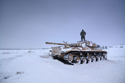 A tank in the snow with one of it crew members standing on it 