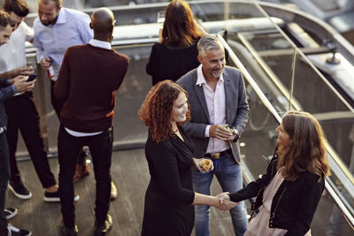 High angle view of businesswoman doing handshake and greeting while partying with coworkers after work on terrace