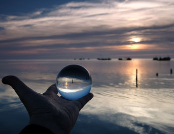 Person holding sunglasses against sea during sunset