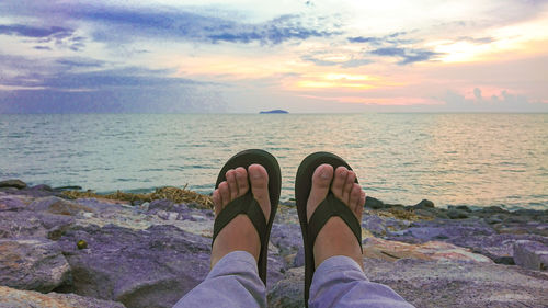 Low section of man in sea against sunset sky