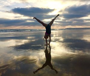 Woman doing handstand at beach against sky during sunset