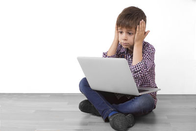 Full length of boy using phone while sitting on floor