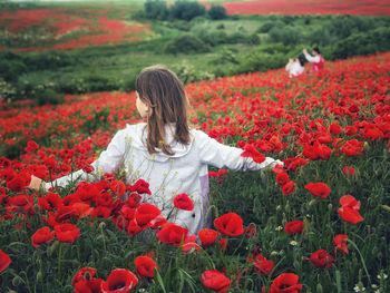 Rear view of woman with red flowers on field